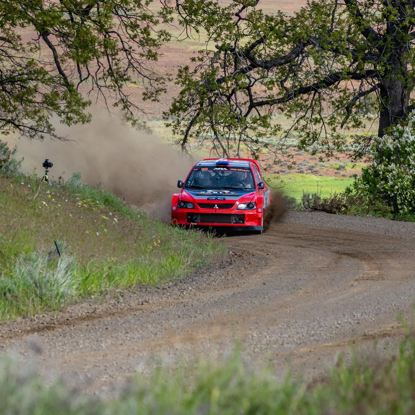 The car cornering on a dusty gravel road through green hills